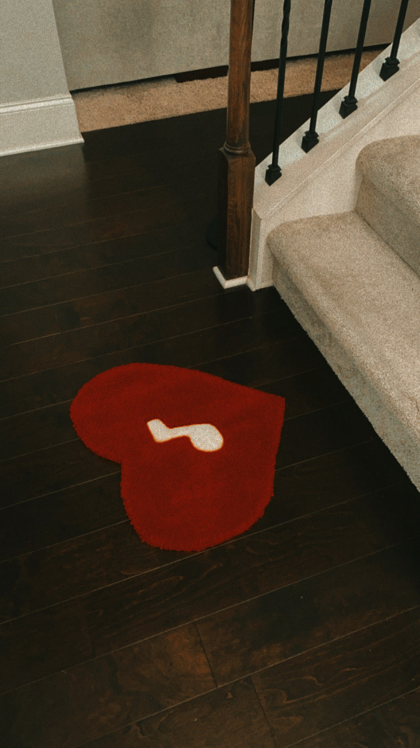Red heart-shaped tufted rug measuring 21 inches by 21 inches, crafted from 100% acrylic yarn, featuring a white music note design at the center.