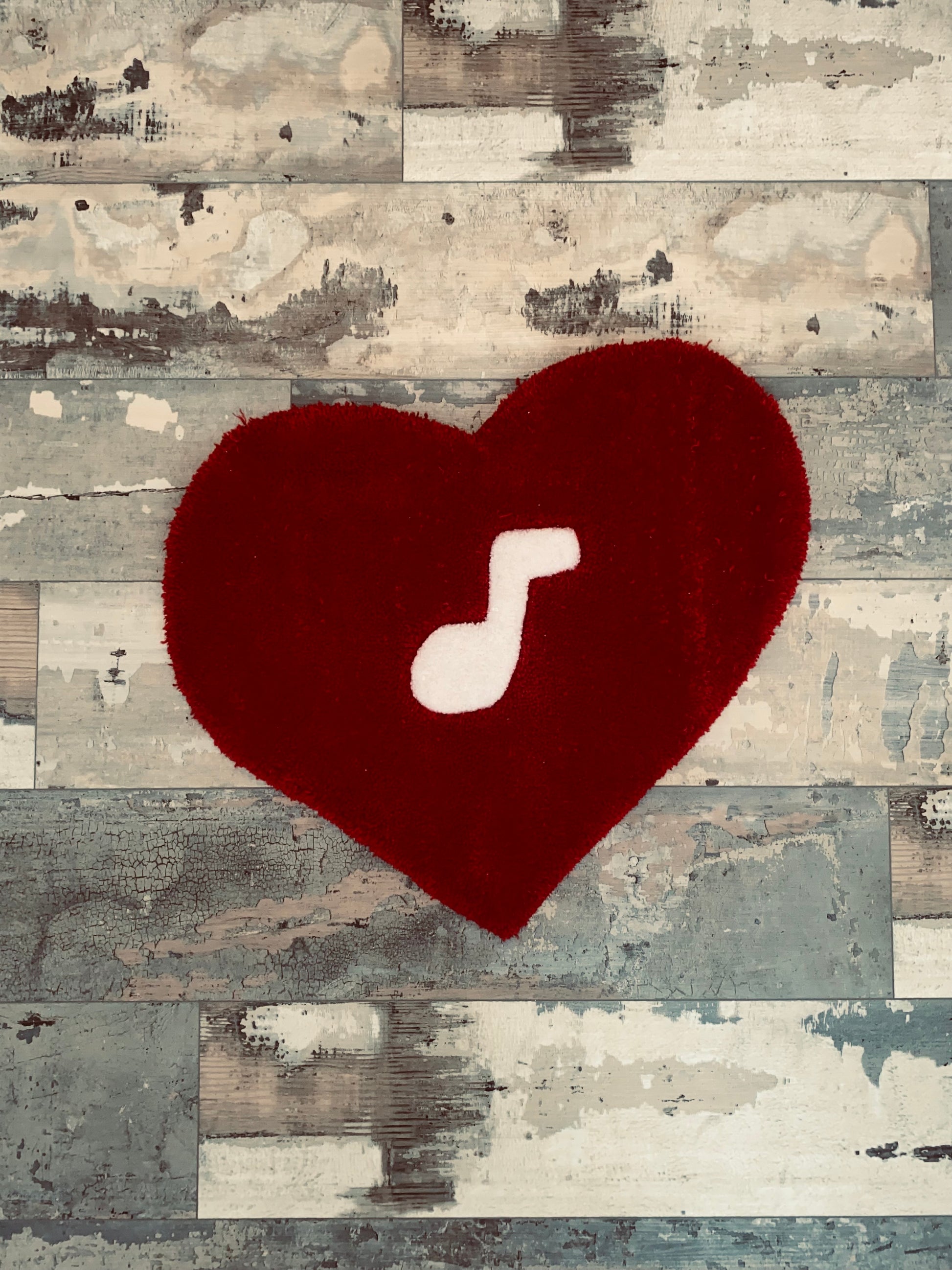 Red heart-shaped tufted rug measuring 21 inches by 21 inches, crafted from 100% acrylic yarn, featuring a white music note design at the center.
